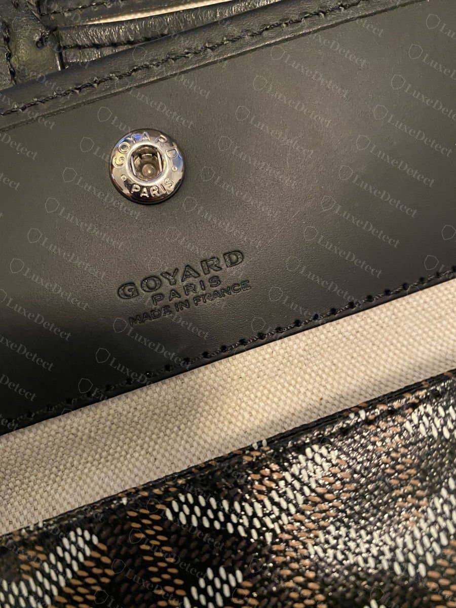 Estampille Goyard Paris Made in France authentique sur le rabat de la pochette en cuir noir, avec des lettres fines et régulièrement pressées sous le bouton-pression