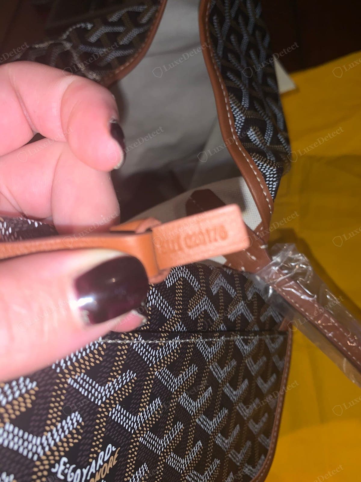 Counterfeit Goyard interior tab — a lot/authenticity code stamped shallow and irregular into pale, plasticky-looking leather, the printed chevron behind it carrying a hard sheen