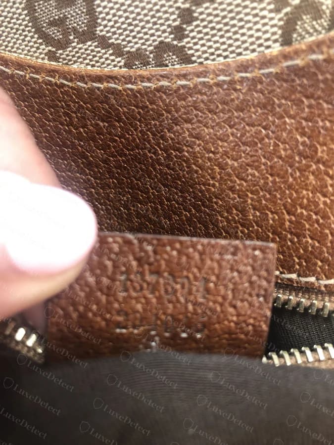 Genuine Gucci serial/style tab, two-line numeric code heat-stamped cleanly into the leather beside the zipper