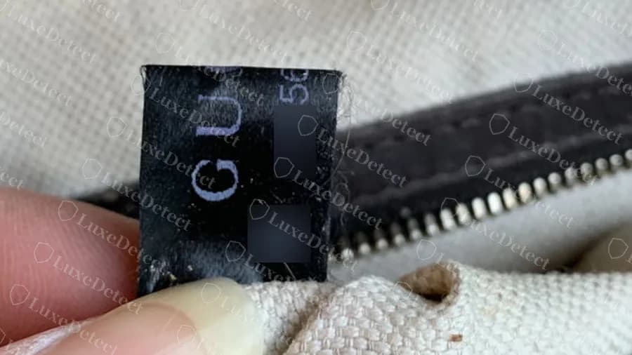 Genuine black fabric label with a small data matrix; the code and matrix are blurred