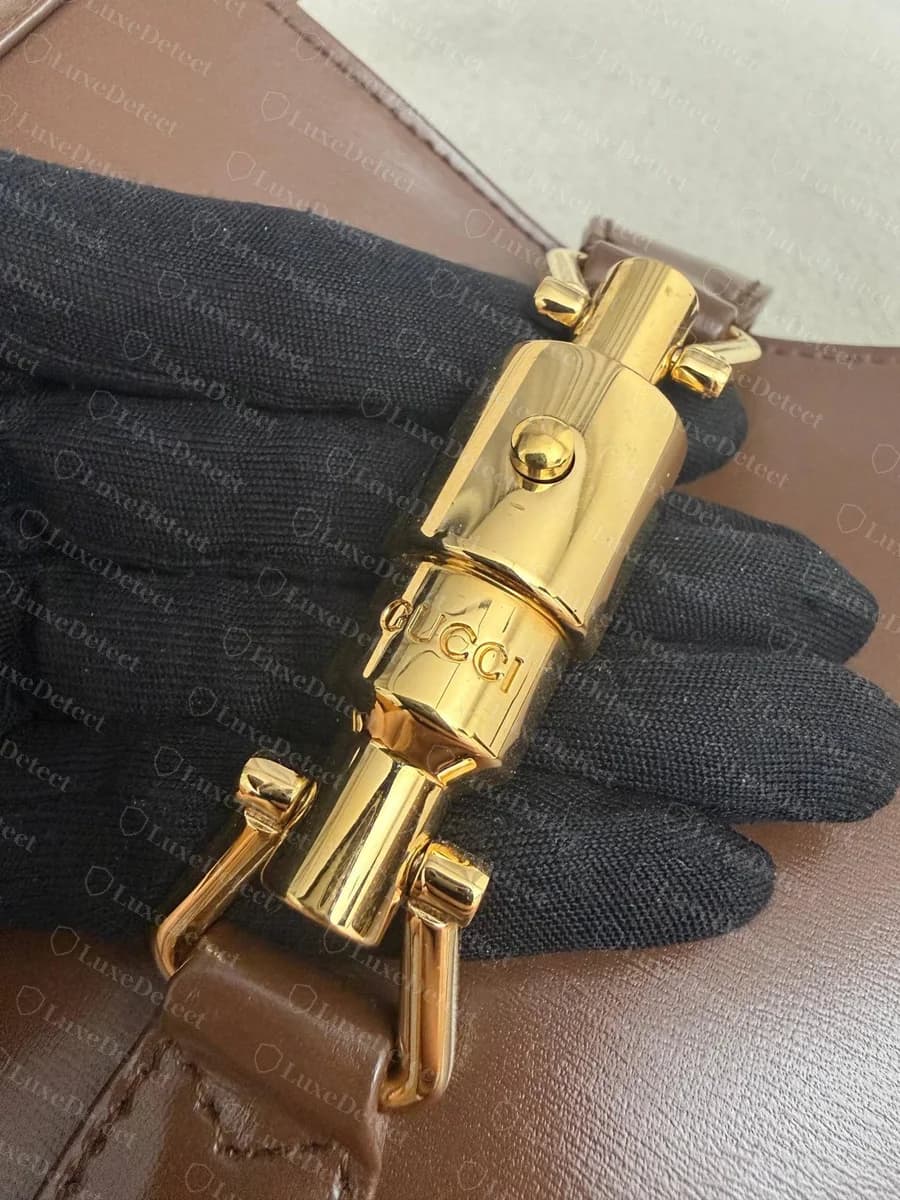 Genuine Gucci Jackie 1961 piston clasp: a warm yellow-gold barrel with the push-button on top, two side lugs and "GUCCI" engraved around the barrel