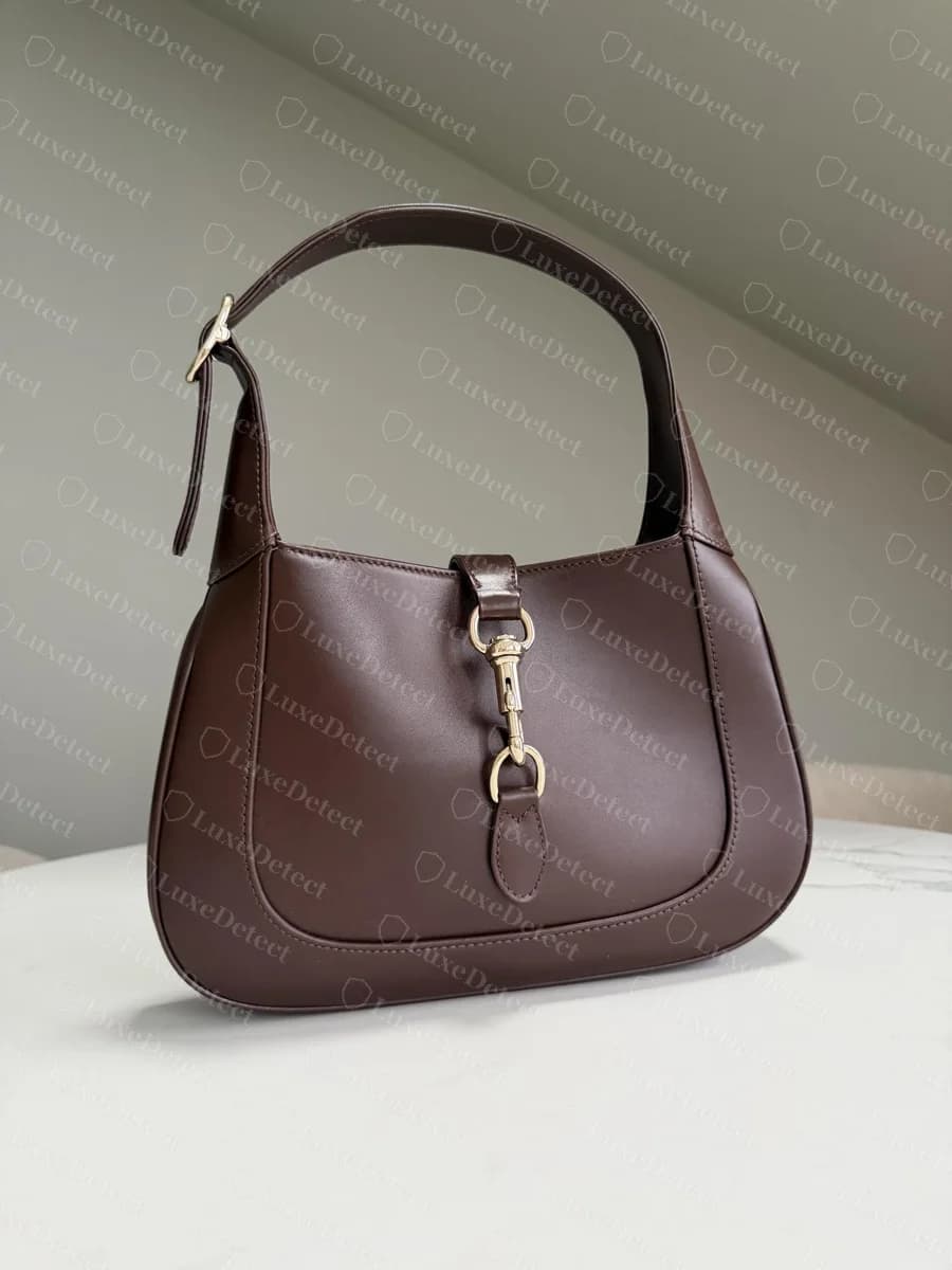 Gucci Jackie 1961 contrefait en cuir marron, vue de face : la même forme en demi-lune, mais un mousqueton à ressort doré pâle pend à la place du fermoir à piston