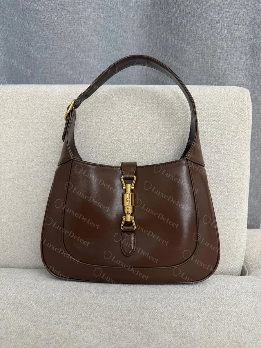Gucci Jackie 1961 pequeño original en piel marrón, vista frontal: el cierre de pistón dorado está en posición vertical en el centro de la pestaña de la solapa y la correa de hombro está abrochada a la izquierda