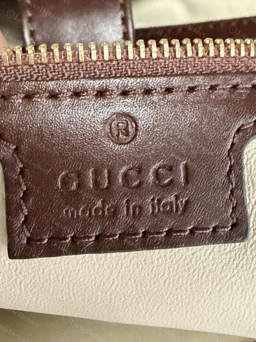 Sello térmico del Gucci Jackie 1961 falso: una marca registrada sobredimensionada y "GUCCI" en letras gruesas e hinchadas, con "made in italy" presionado a fondo y borroso, de modo que las letras se pegan entre sí