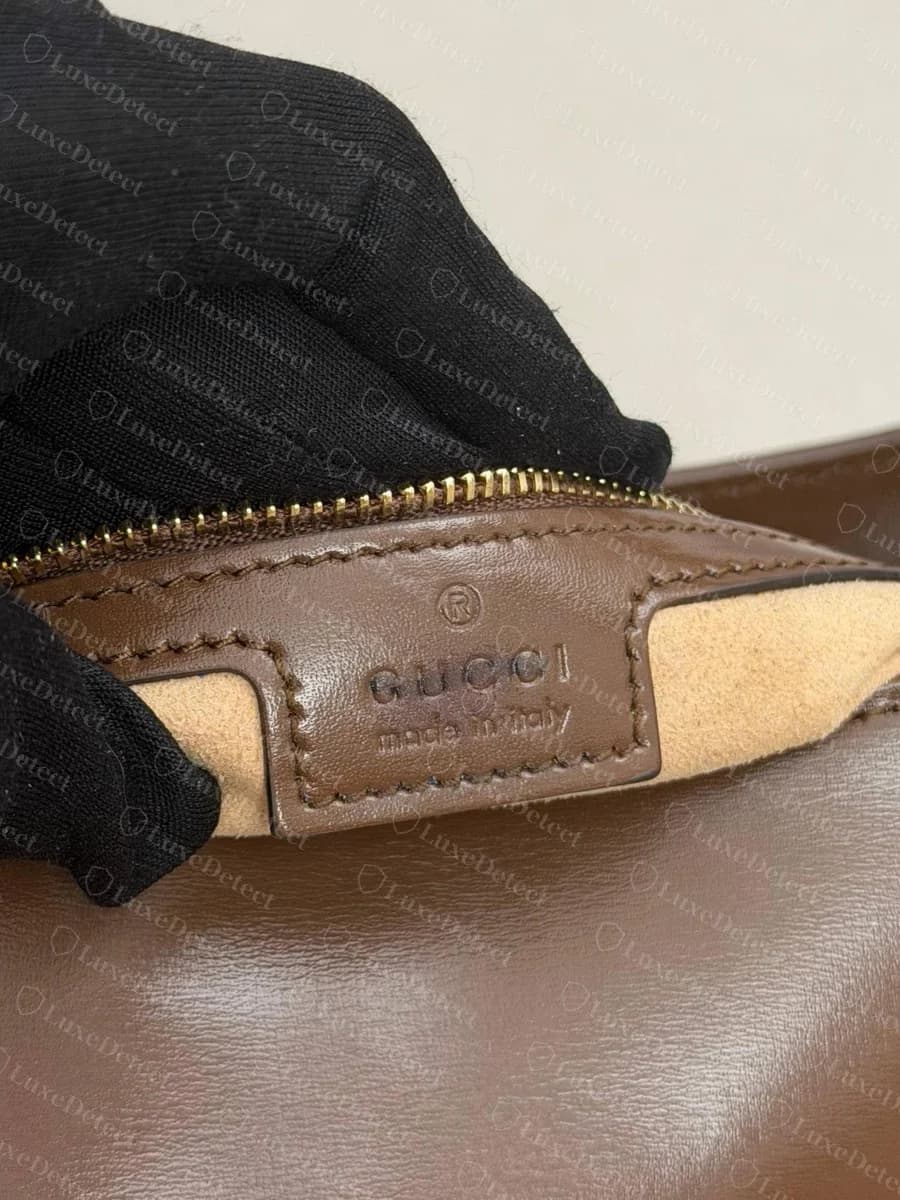 Sello térmico del Gucci Jackie 1961 original: una pequeña marca registrada sobre "GUCCI" y "made in Italy" en letras finas y delgadas, presionadas de forma poco profunda y pareja en la pestaña de piel beige