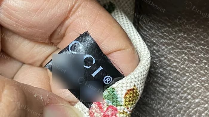 Genuine black fabric tag with spaced capital letters and the registered mark, sewn into the lining of a Neo Vintage crossbody (code and data-matrix block blurred)