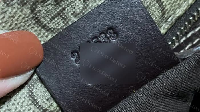 Genuine leather interior tag on a flat GG Supreme messenger, a six-digit model number over a six-digit production number, evenly debossed (production line blurred)