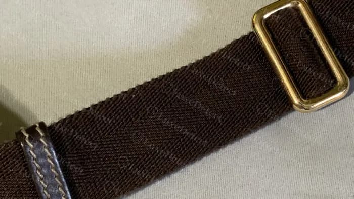 Genuine plain brown woven strap with a gold-tone slide and a stitched leather keeper on a flat GG Supreme messenger