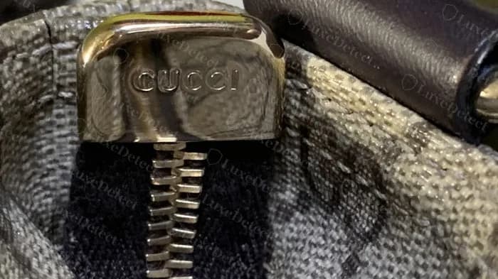 Genuine polished zip slider cap engraved GUCCI in clean serif capitals on a flat GG Supreme messenger