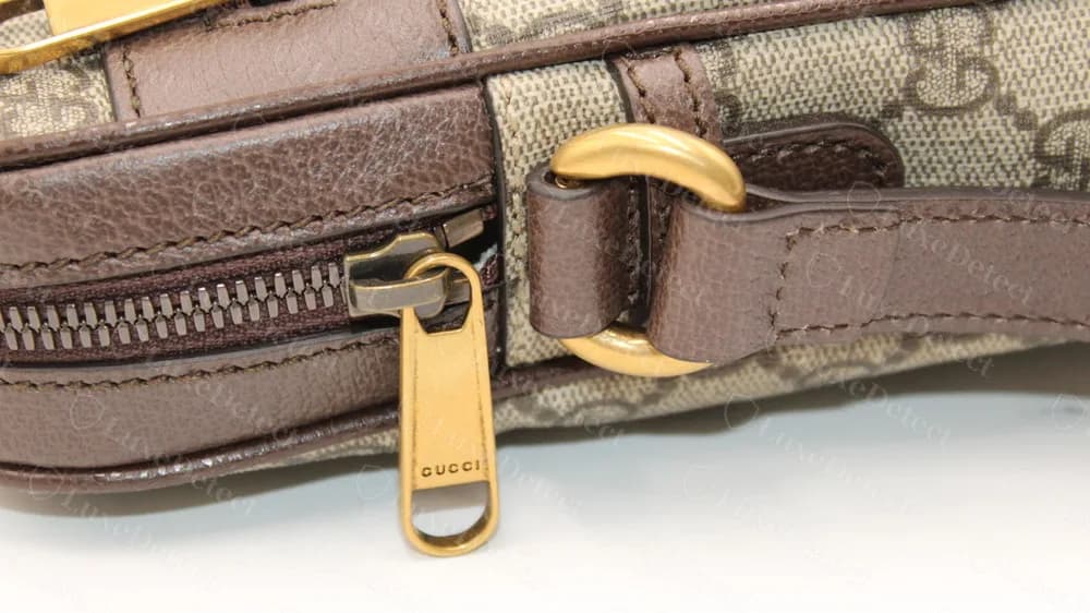 Genuine antique-gold zip pull engraved GUCCI beside a leather-wrapped strap ring on an Ophidia messenger