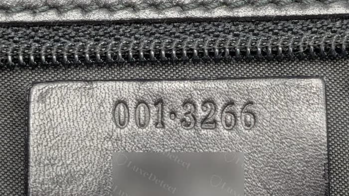 Pestaña de piel Gucci antigua genuina que muestra un número de modelo con punto sobre un número de producción de seis dígitos, estampados de forma uniforme en una pestaña de piel cosida en el forro (segunda línea difuminada)