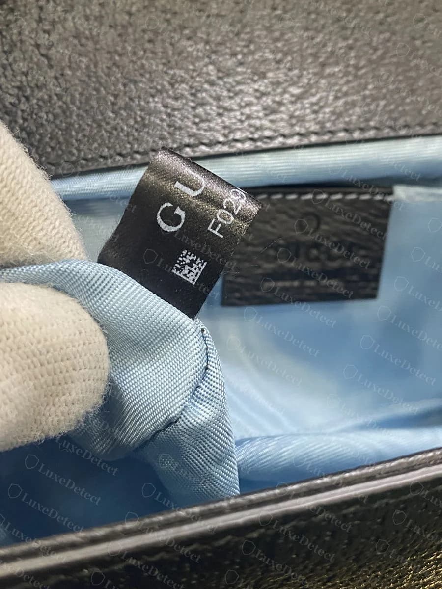 Genuine interior, showing the satin ribbon serial tag and the separate embossed leather "GUCCI made in Italy" patch sewn in nearby, both legitimate on the same bag
