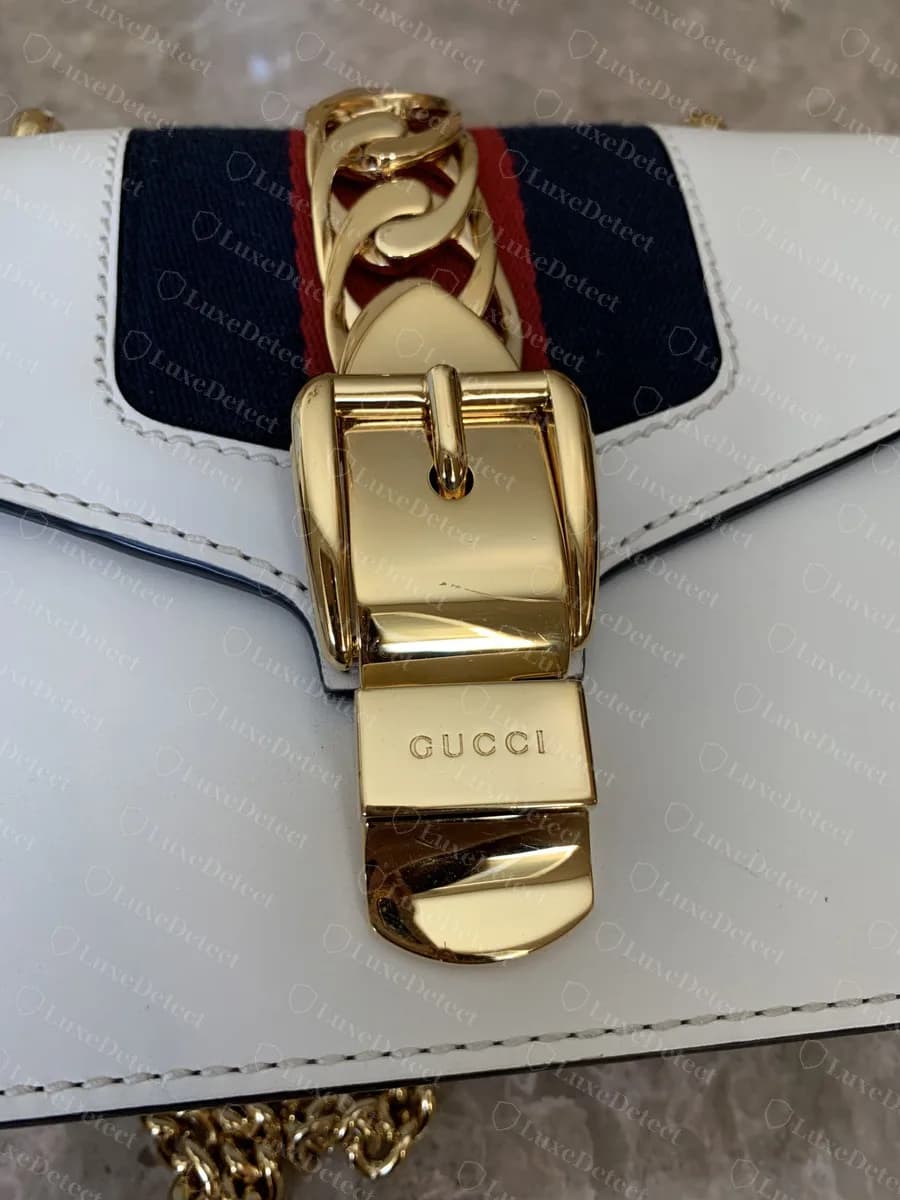 Genuine Sylvie buckle and hinged tongue plate, "GUCCI" engraved in small evenly spaced capitals above the curved polished lip