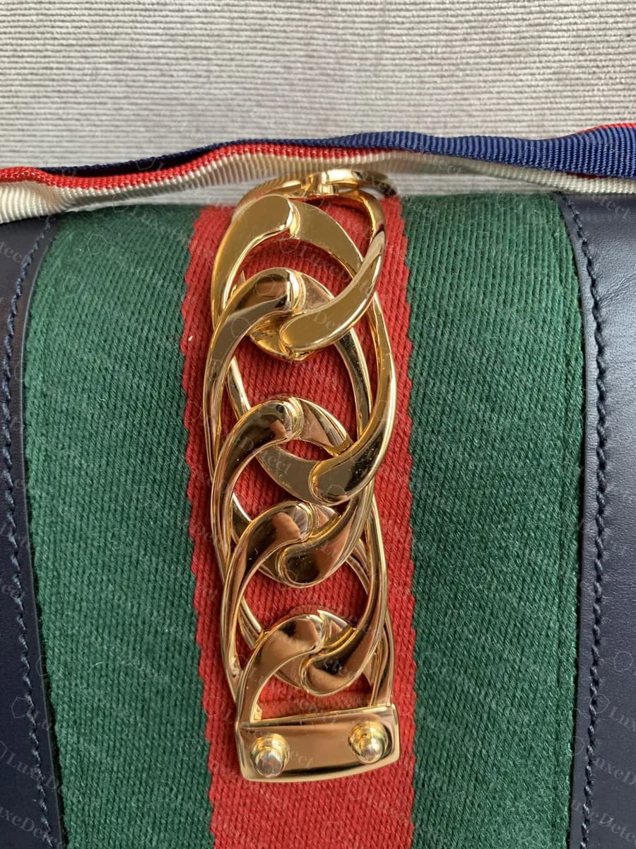 Genuine Gucci Sylvie curb chain over green-red-green web on navy leather, showing the polished overlapping links and the two-rivet anchor plate at the base
