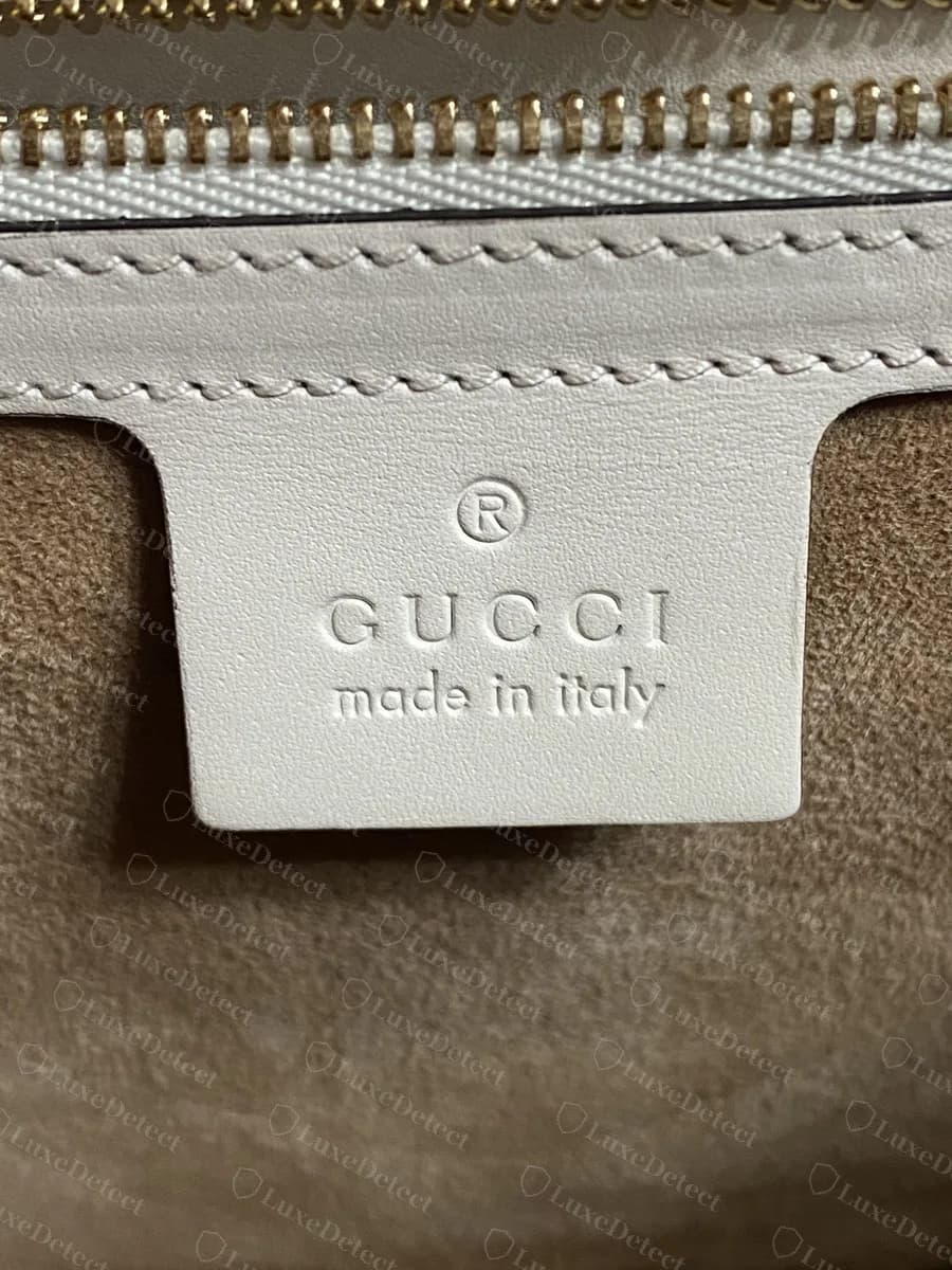 Genuine Sylvie interior heat stamp on white leather: ®, "GUCCI" and "made in italy" evenly pressed, with neat stitching around the tab