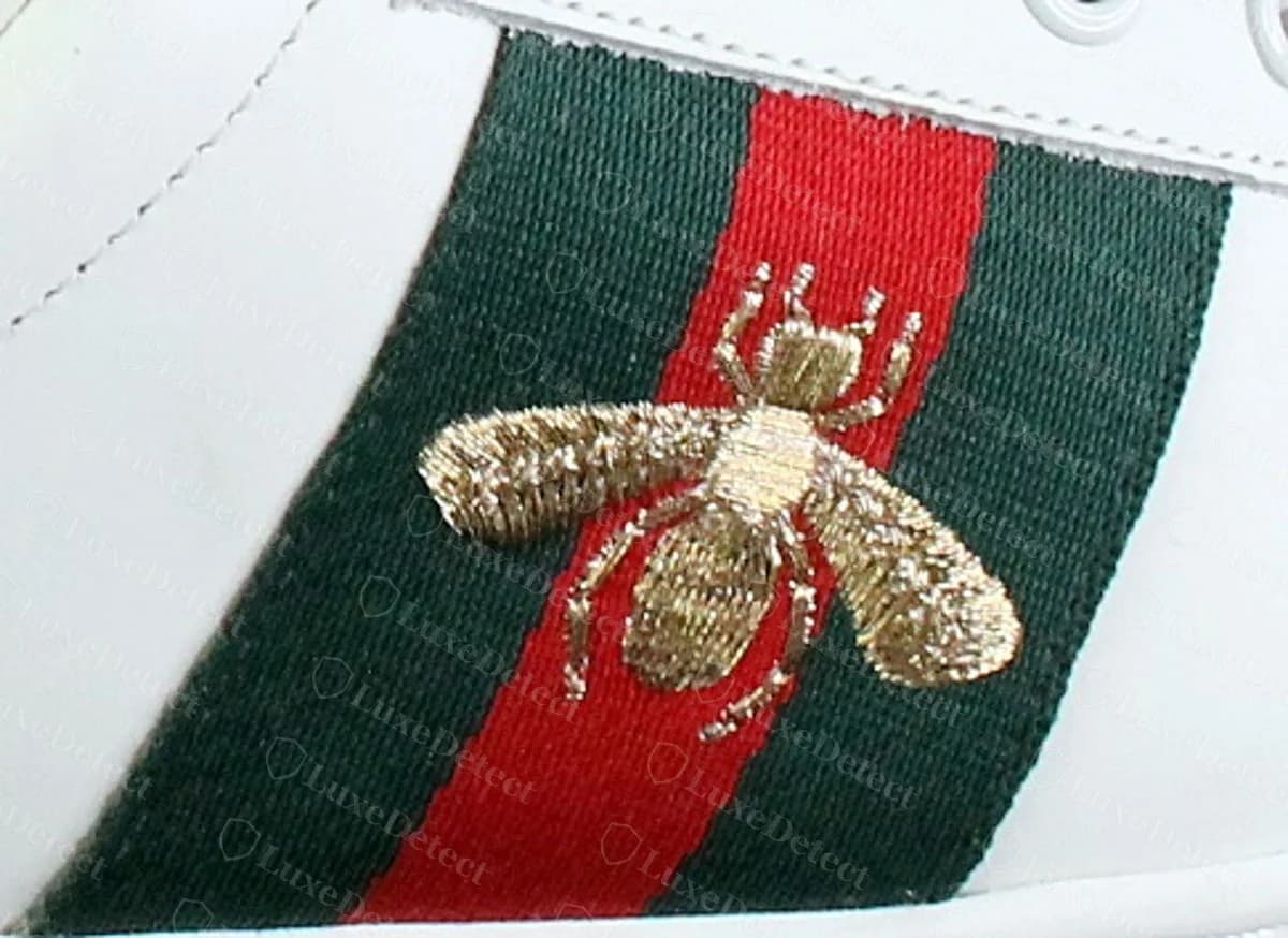 Counterfeit Gucci Ace bee — coarse, raised gold stitching, fuzzy wing tips with loose thread ends, legs ending in blobby knots
