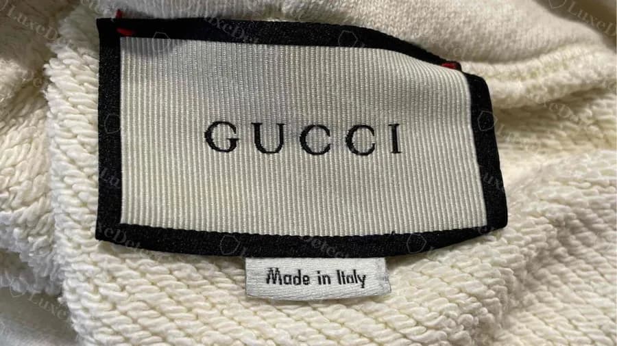 Una sudadera Gucci falsa con una etiqueta crema convincente en el cuello y una subetiqueta Made in Italy que copia el diseño original