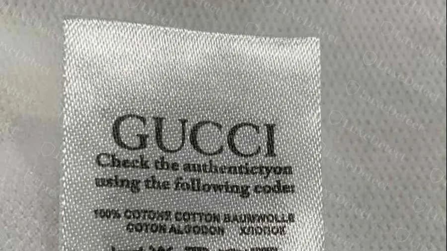 Gefälschtes Gucci T-Shirt: ein QR-Code-Etikett mit falsch geschriebener Echtheitszeile und wirrem Fasertext