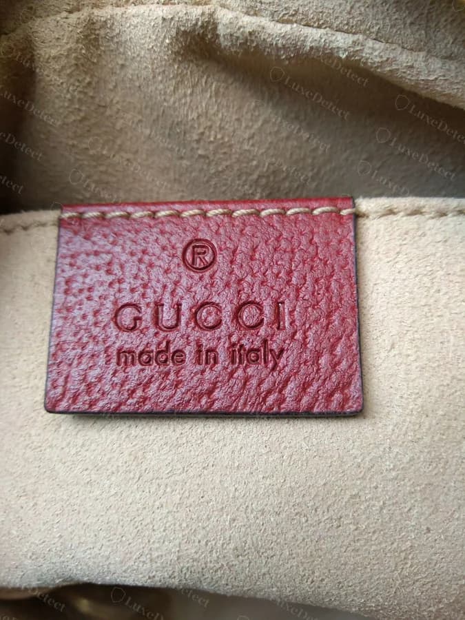 Authentic Gucci interior control tag on a Flora piece, heat-stamped leather reading GUCCI made in Italy with a registered trademark mark, fully legible and cleanly cut