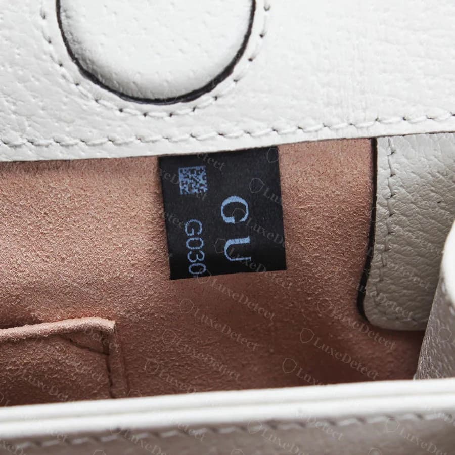 Counterfeit Flora bag interior label, cropped so the GUCCI wordmark reads only GU and the style code is cut off after a few characters, as if the label was trimmed to the wrong size