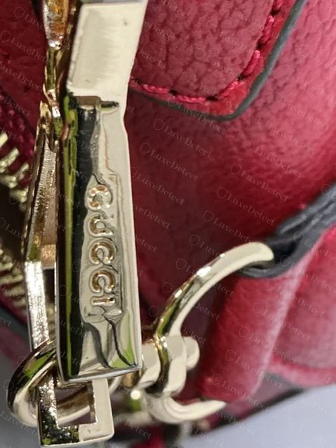Counterfeit Gucci zipper pull stamp, the GUCCI lettering visibly uneven in size and spacing compared to a genuine stamp