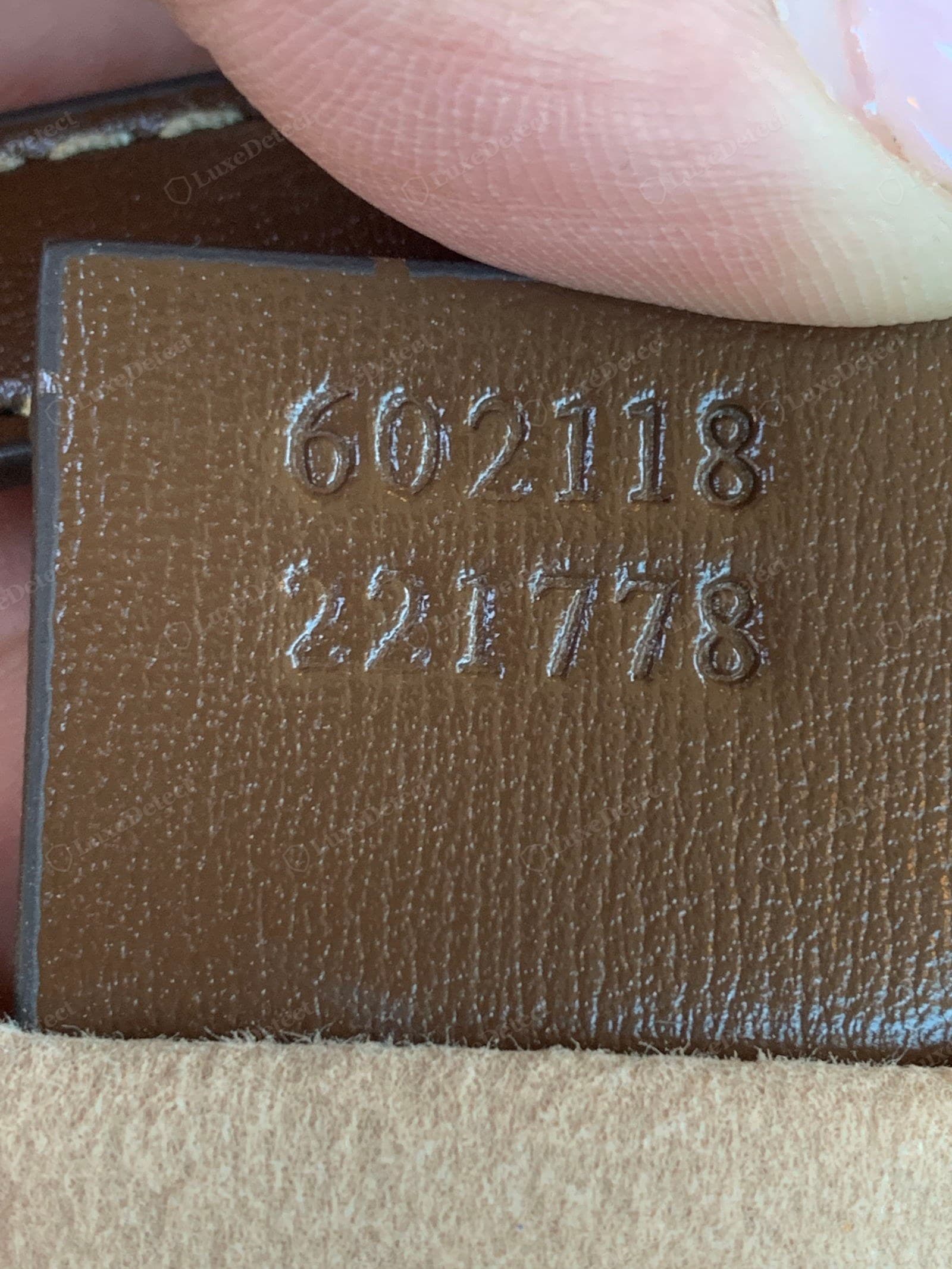 Counterfeit Gucci Horsebit 1955 serial tab — the two-line numeric code heat-stamped unevenly, the numbers soft and printed-looking