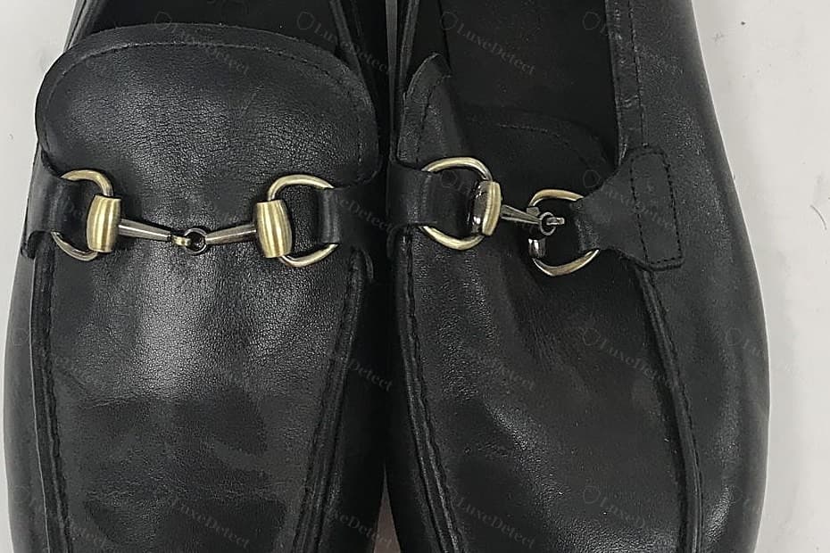 Counterfeit Gucci Horsebit hardware — a mismatched finish with antiqued-brass rings against darker gunmetal bar links, a thin crude casting, the bit hanging loose in the keepers