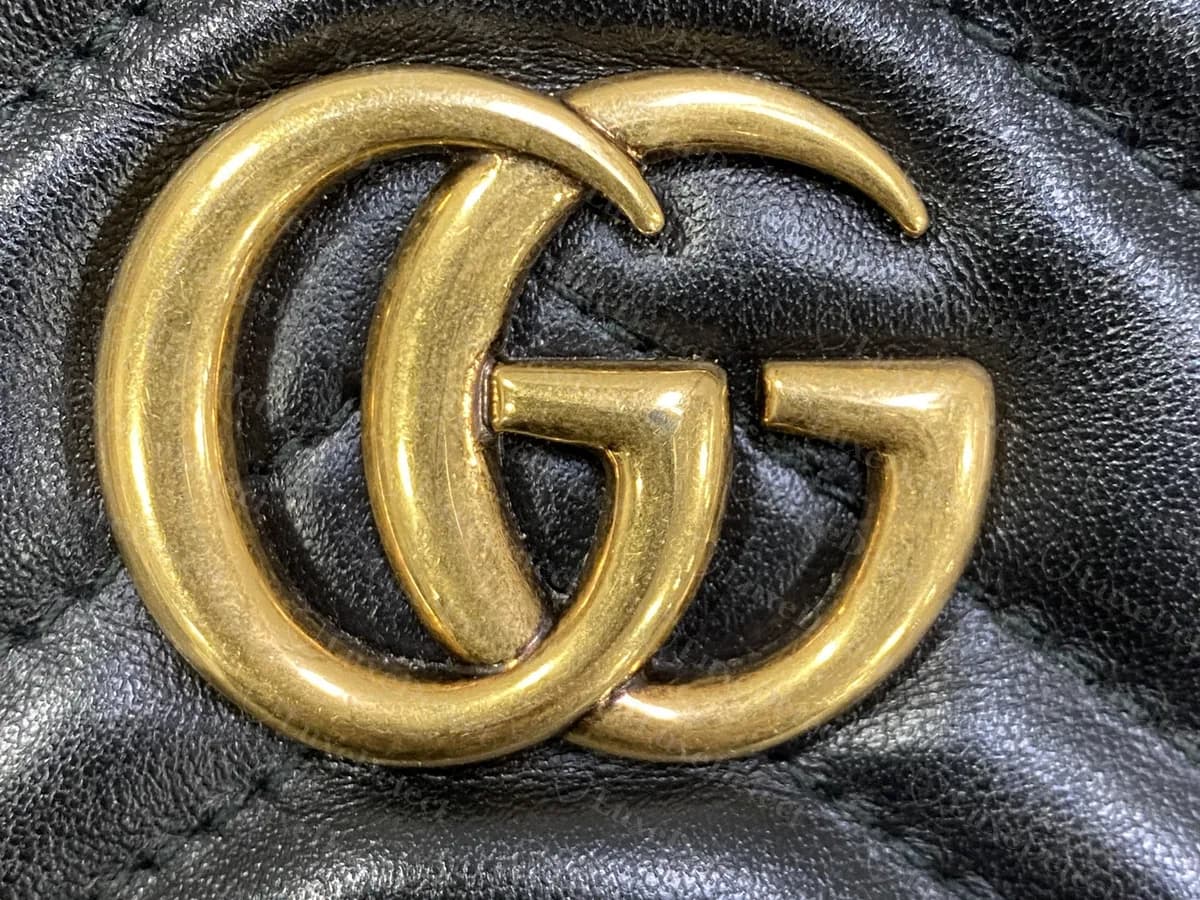 Close-up of the antique-gold double-G on a genuine black Marmont, the two Gs overlapping with rounded, evenly thick strokes and a warm brass tone