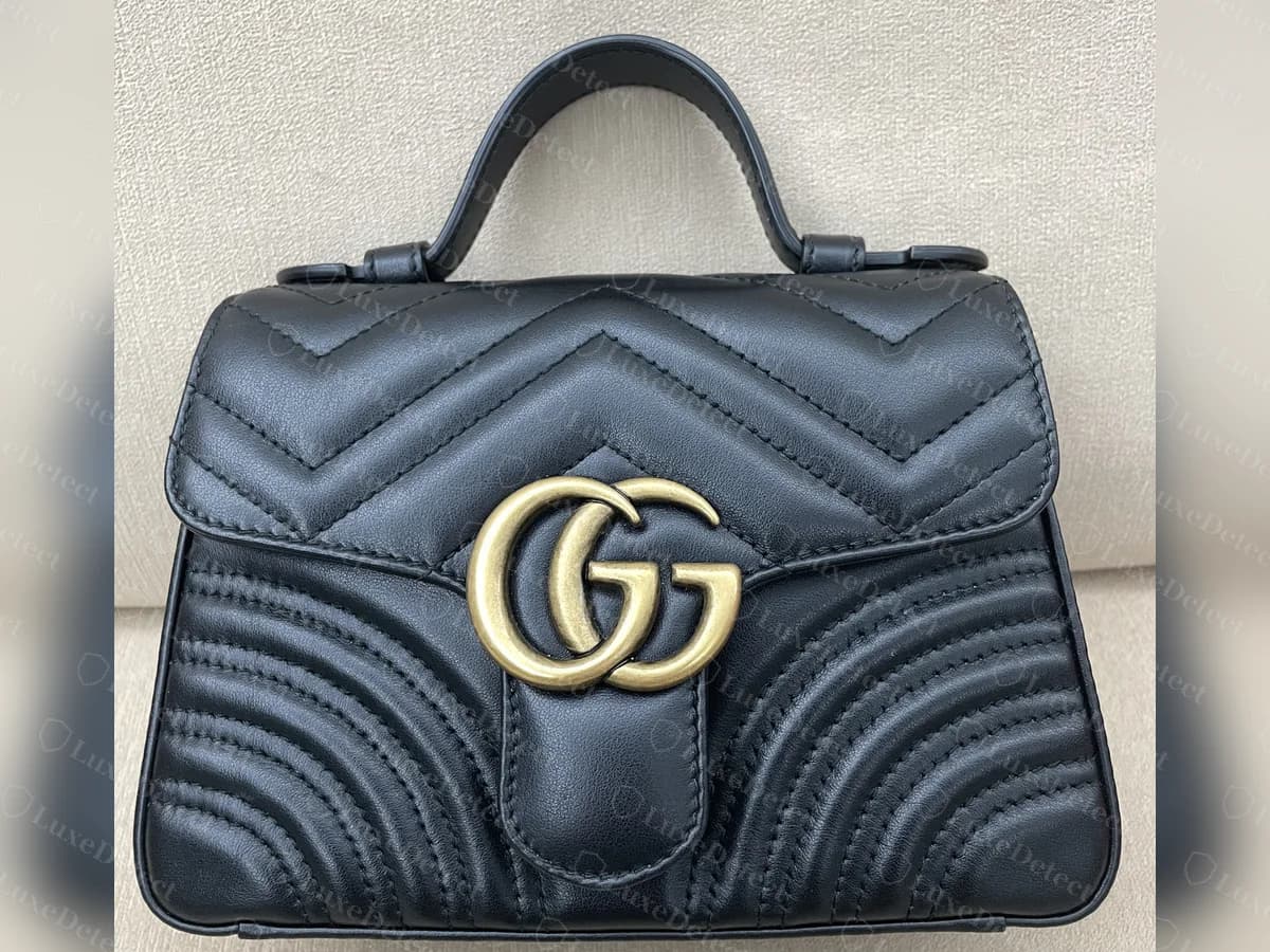 Genuine black GG Marmont top-handle mini bag from the front: a chevron-quilted flap with an antique-gold double-G on a leather tab, a single top handle and curved quilting on the lower front