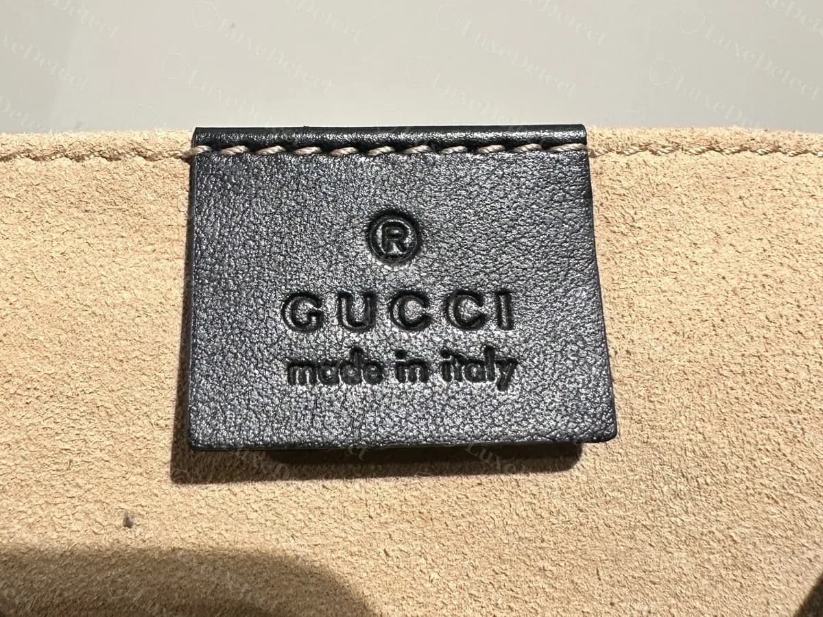 Frente de la etiqueta interior de piel de un Marmont original: una marca registrada sobre GUCCI en mayúsculas y "made in Italy" en minúsculas, prensados en piel negra