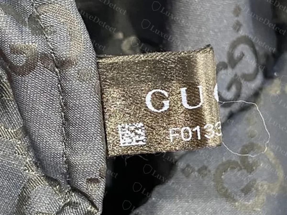Etiqueta negra de tela Gucci original cosida al forro con el logotipo GUCCI, un pequeño bloque QR y un número que empieza con la letra F