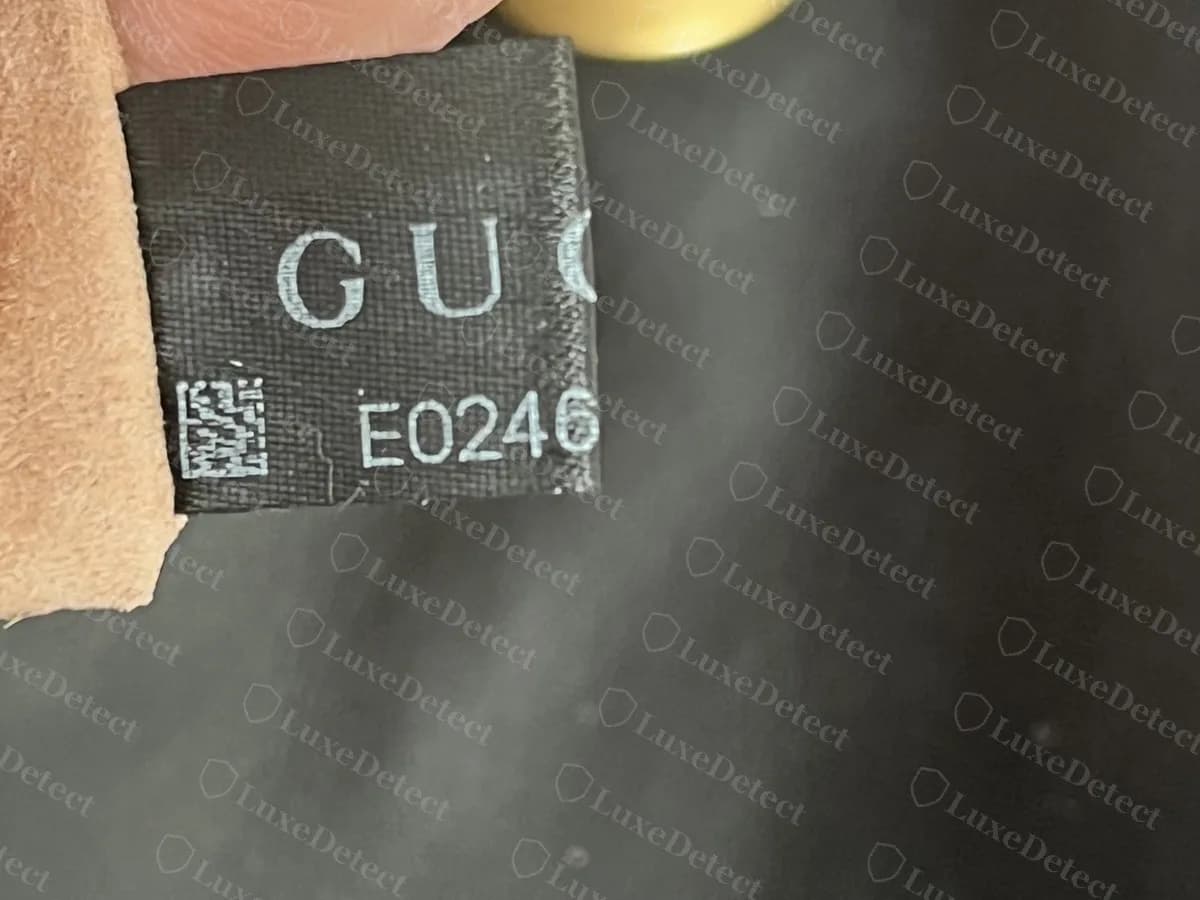 A black fabric label with a QR block and the number E0246 on a counterfeit Marmont, copying the genuine layout