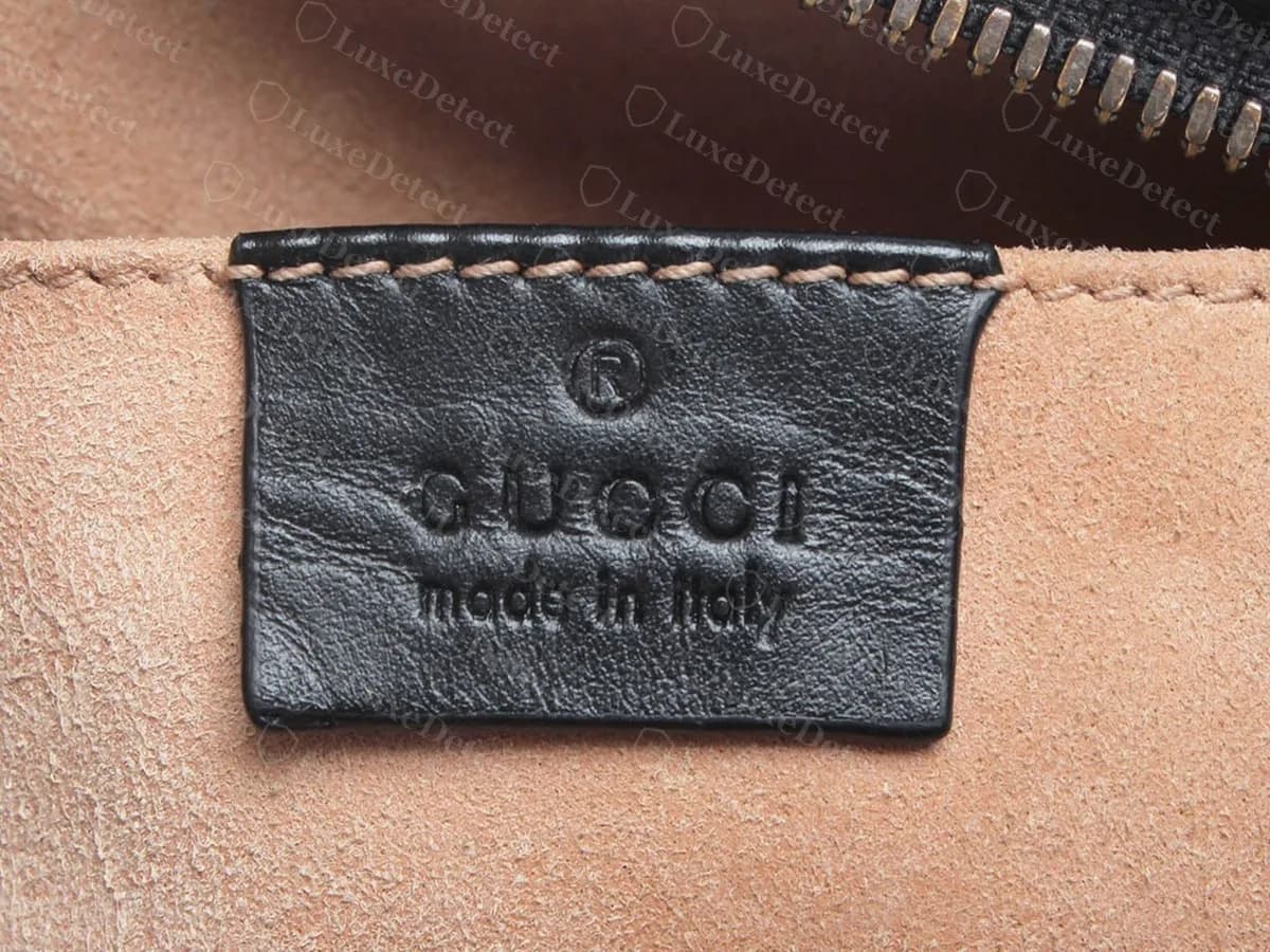 Front of a genuine Gucci interior tag in black leather: a registered mark, GUCCI in capitals and made in Italy in lower case, with stitched edges