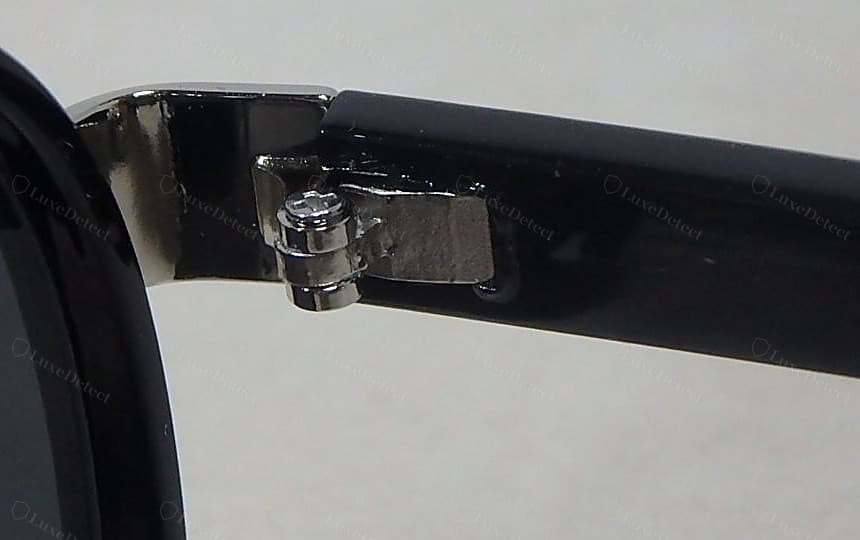 Bisagra Gucci falsificada: una placa de bisagra fina y estampada con adhesivo oscuro untado en la unión con el acetato y un pasador a presión tosco en lugar de un tornillo ranurado