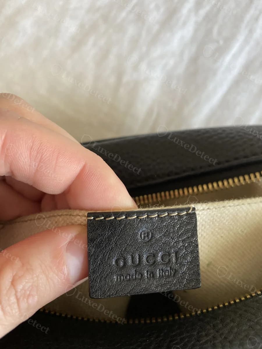 Counterfeit Gucci Soho Disco interior leather stamp, black leather panel reading GUCCI made in Italy, held open against the bag's canvas lining