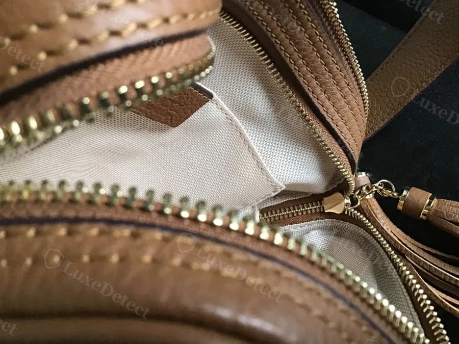 Counterfeit Gucci Soho Disco tassel cap, tan leather, gold-tone cap visible at the base of the tassel next to the open zipper