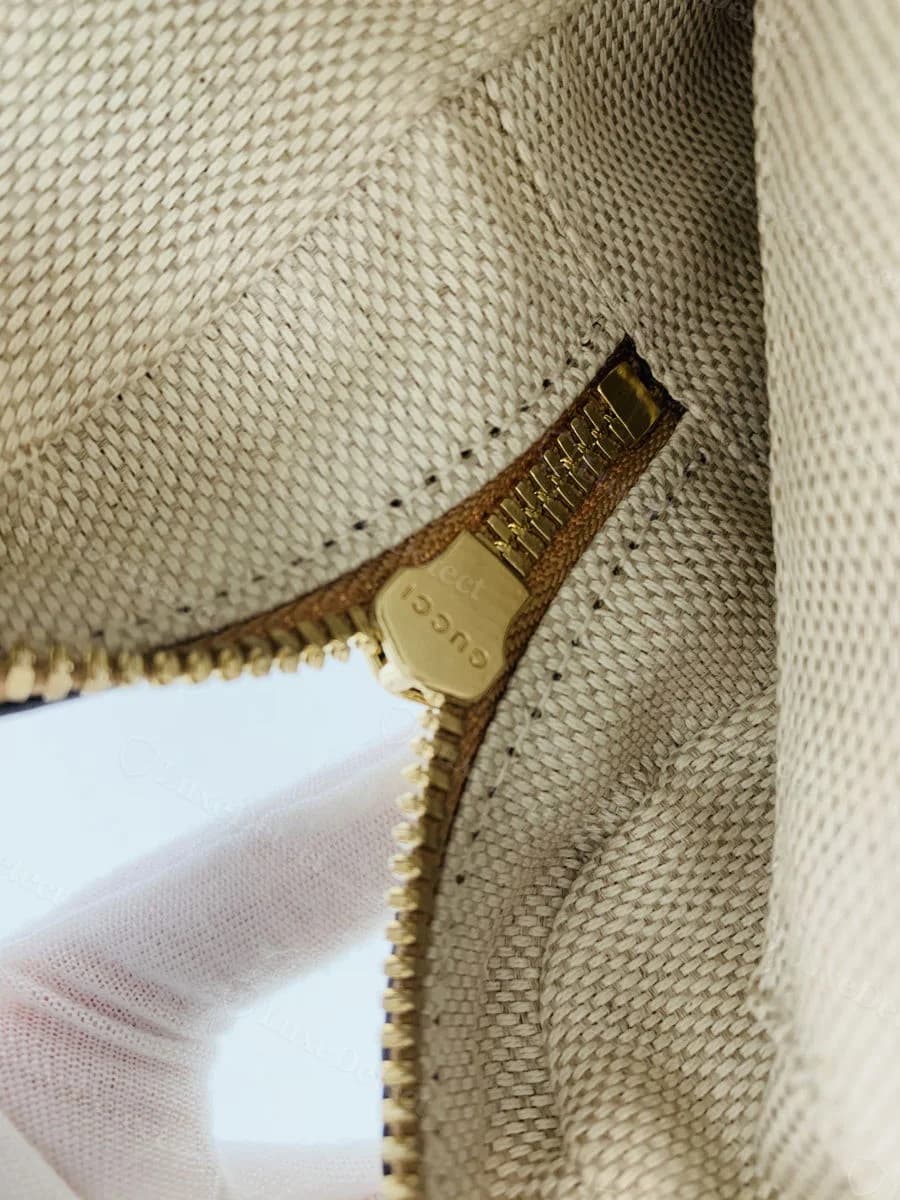 Authentic Gucci Soho Disco zipper pull, gold shield-shaped tab stamped GUCCI in block capitals, shown open against the canvas lining