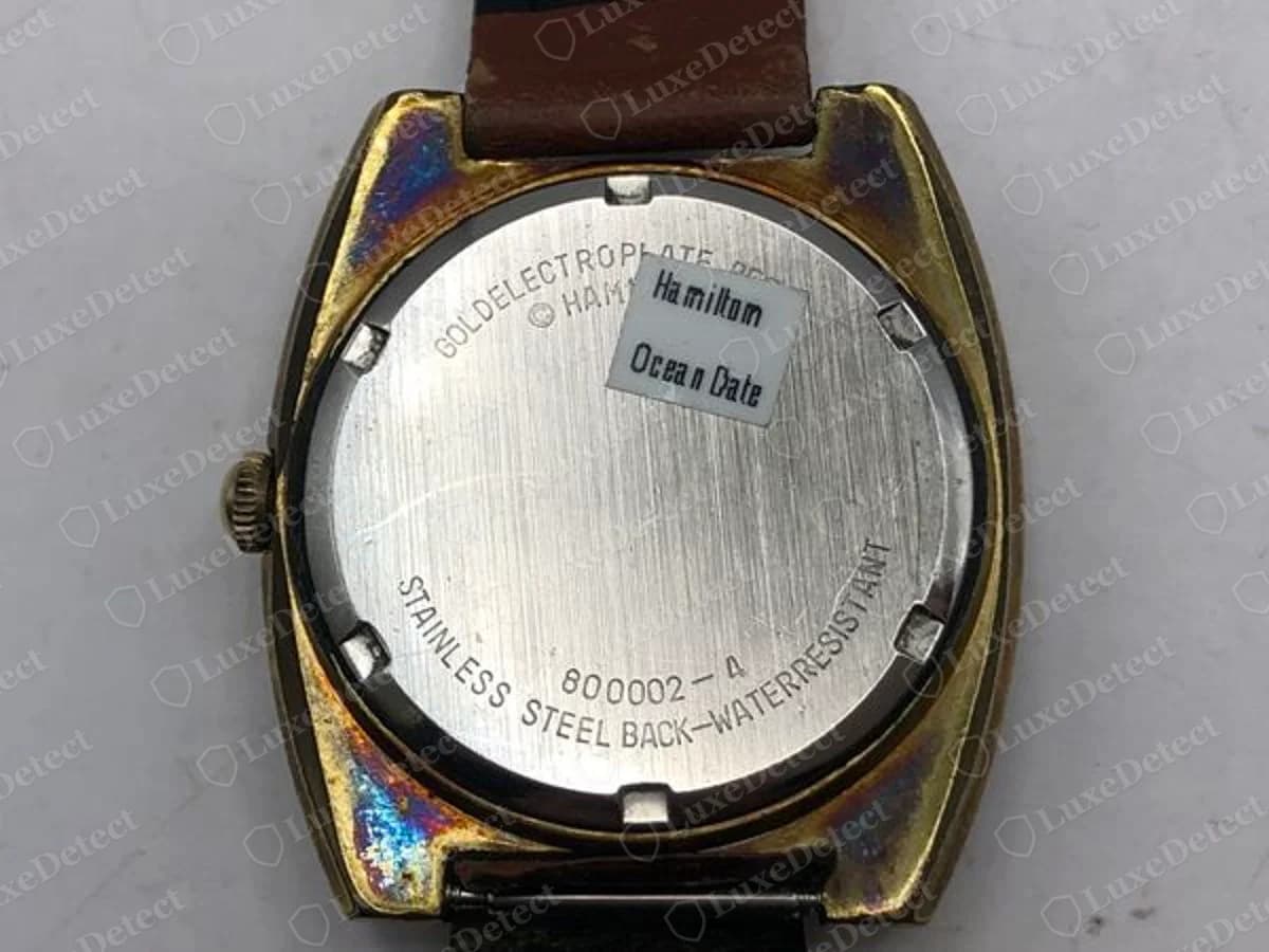 Back of a genuine vintage Hamilton Ocean Date watch with a gold-coloured case, showing GOLD ELECTROPLATE, a partly legible Hamilton copyright line, STAINLESS STEEL BACK WATERRESISTANT, the number 800002-4 and a small white sticker reading Hamilton Ocean Date