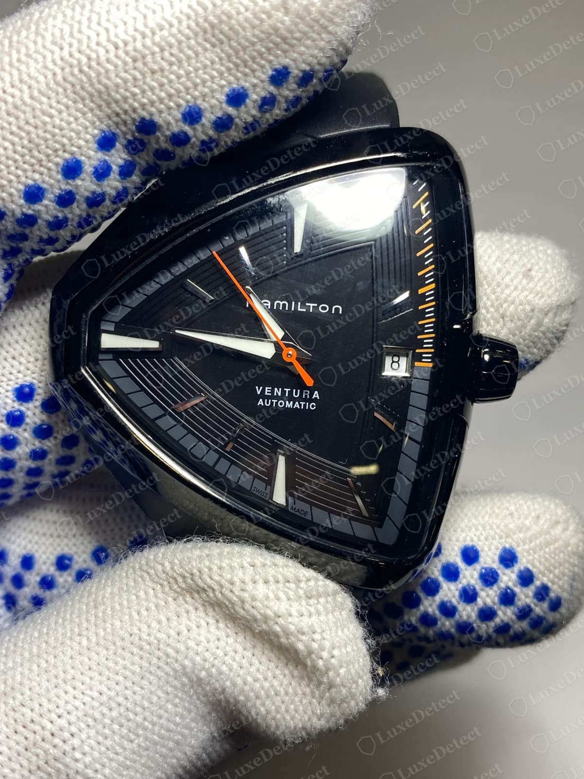 Genuine black Hamilton Ventura triangular watch with HAMILTON above VENTURA AUTOMATIC on the dial, an orange seconds hand, a date window at the right and SWISS MADE printed at the bottom of the dial