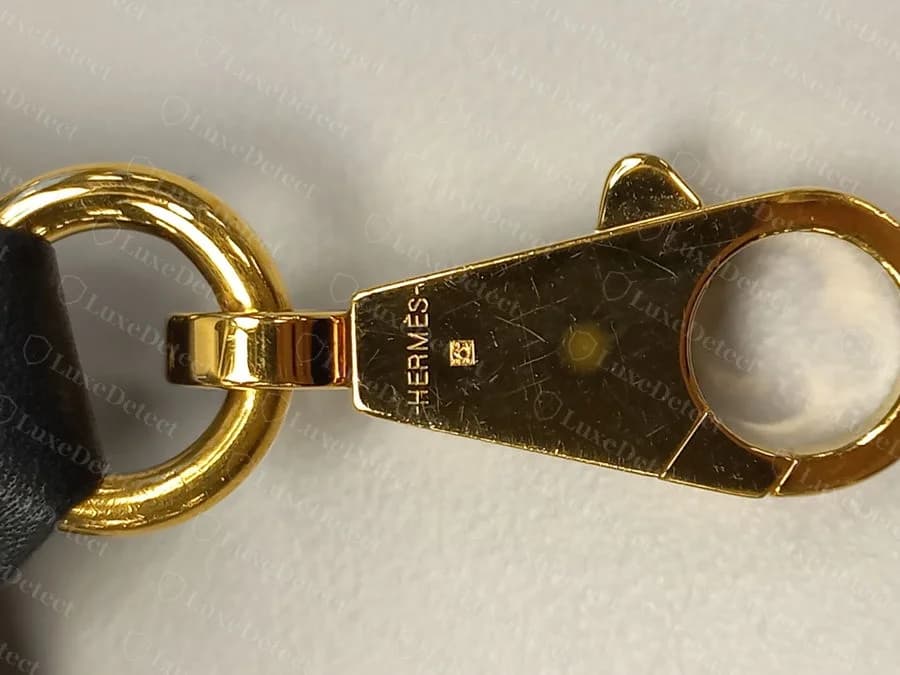 Genuine Hermès Bolide zipper-pull tab, gold-tone HERMÈS engraving with the small craftsperson's-mark square beside it