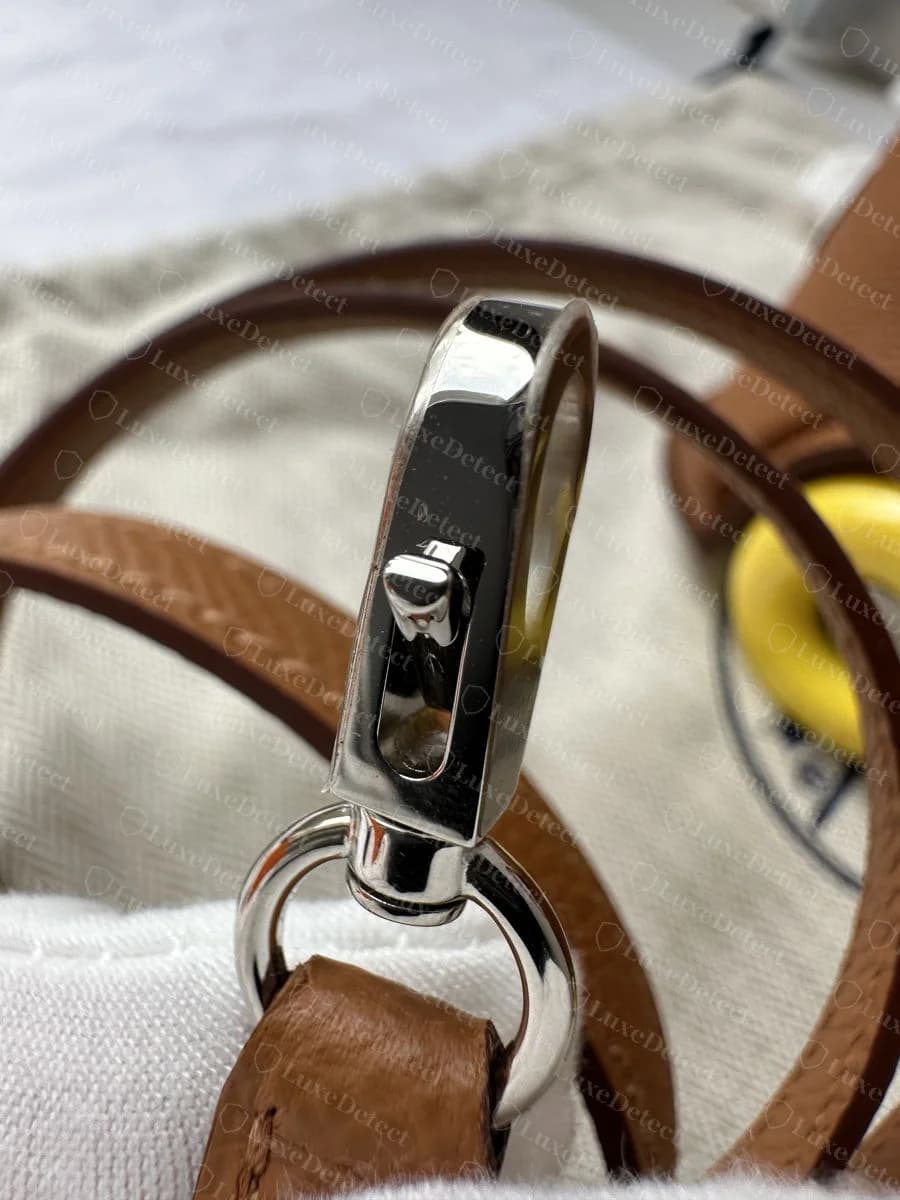 Hermès Bolide shoulder-strap clip, a polished silver-tone swivel hook stamped HERMÈS along its face, attached to the tan leather strap