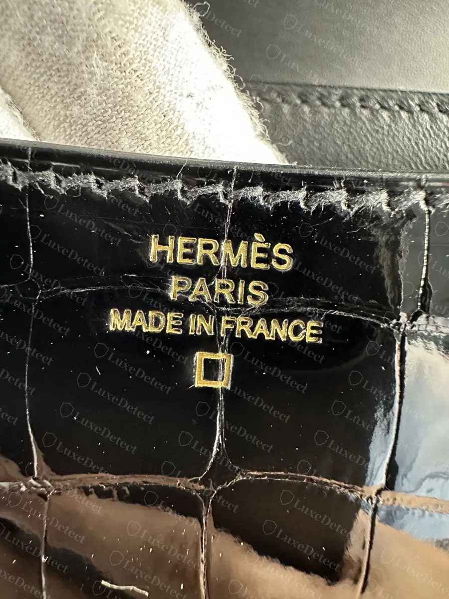 Gold-foil stamp on shiny black alligator, the square alligator symbol on its own line below MADE IN FRANCE