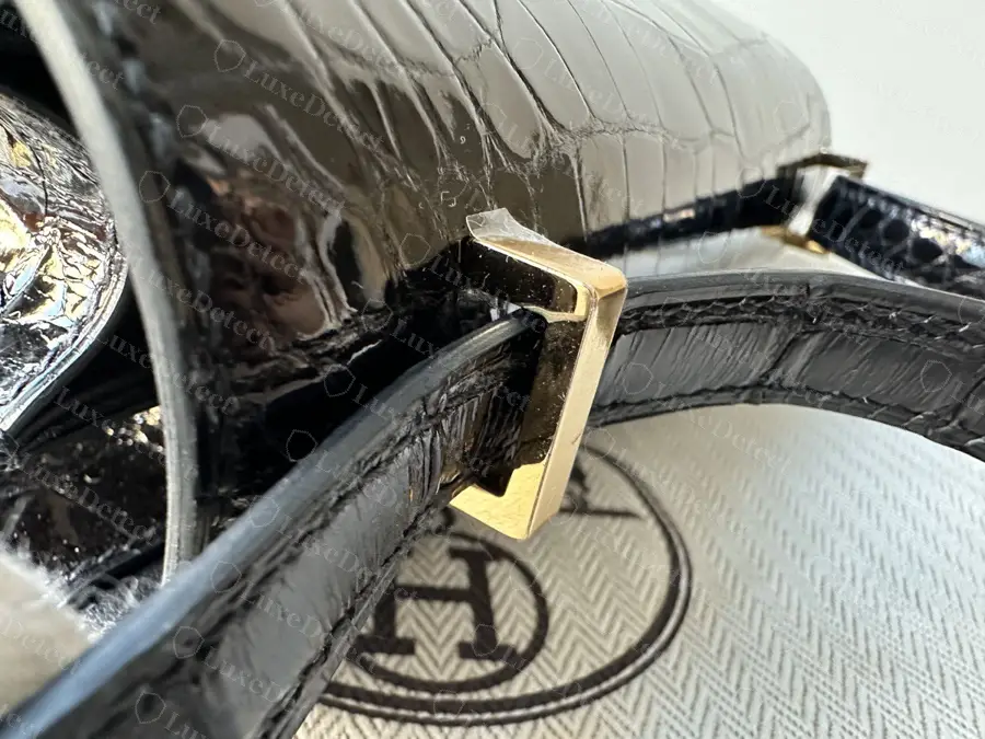 Strap passing through the gold rectangular side loop on a shiny black alligator Constance