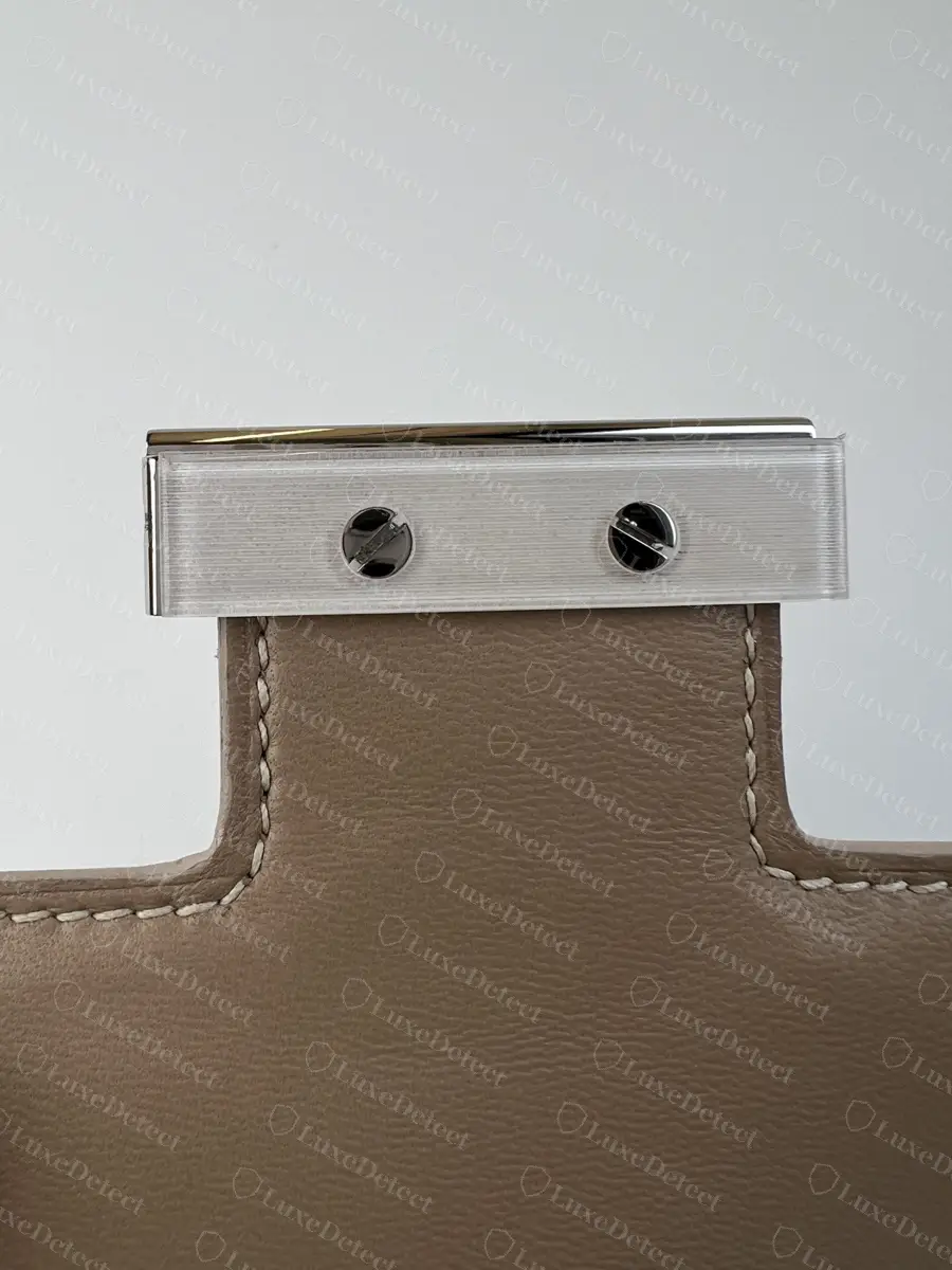 Inner face of the centre-bar piece on a genuine Constance tab: brushed metal plate, two slotted screws, even stitching around the T-shaped leather tab