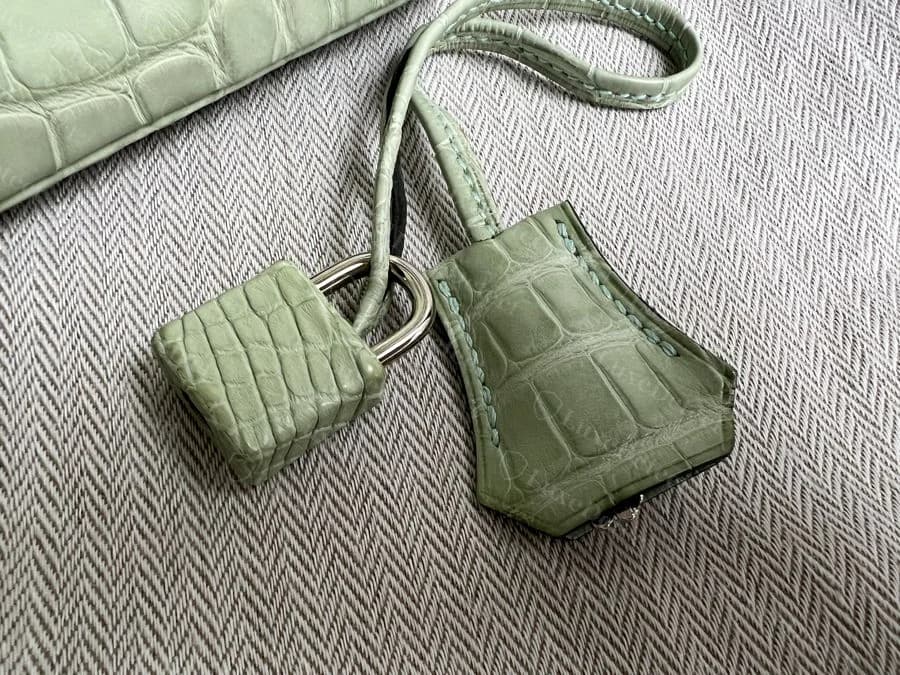 Genuine alligator padlock and clochette set, scale pattern continues cleanly around the padlock's curved face and matches the bag's main panel
