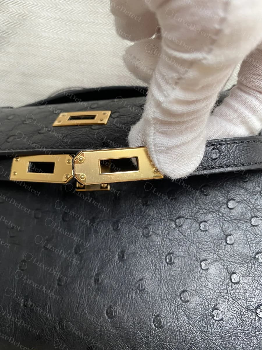 Genuine ostrich Kelly turn-lock plate, crisp HERMÈS PARIS engraving with the small craftsman's mark square beside it