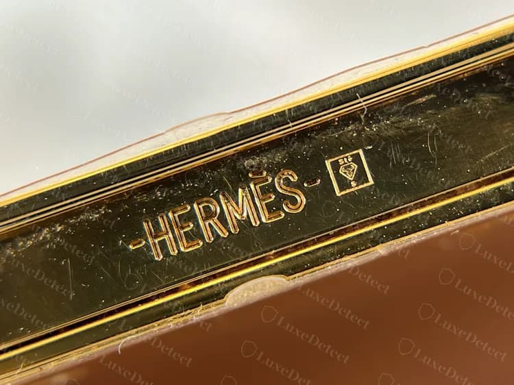 Borda da ferragem de uma Constance Slim original gravada -HERMÈS- seguida de uma pequena marca, em dourado