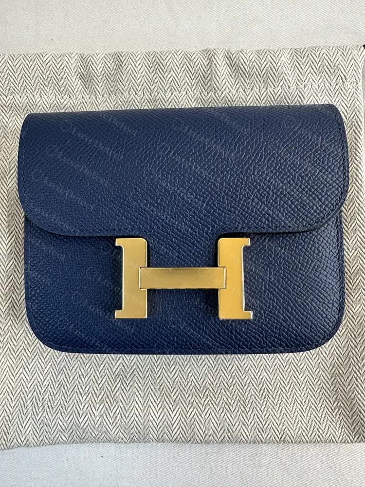 Carteira Hermès Constance Slim original em Epsom azul com fecho H dourado, fotografada sobre o dust bag