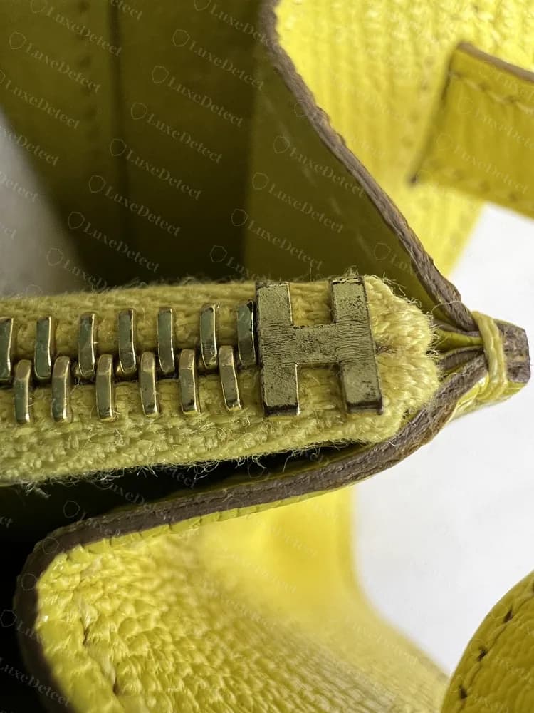 Zíper de uma Kelly To Go original com um pequeno puxador em forma de H, sobre forro amarelo