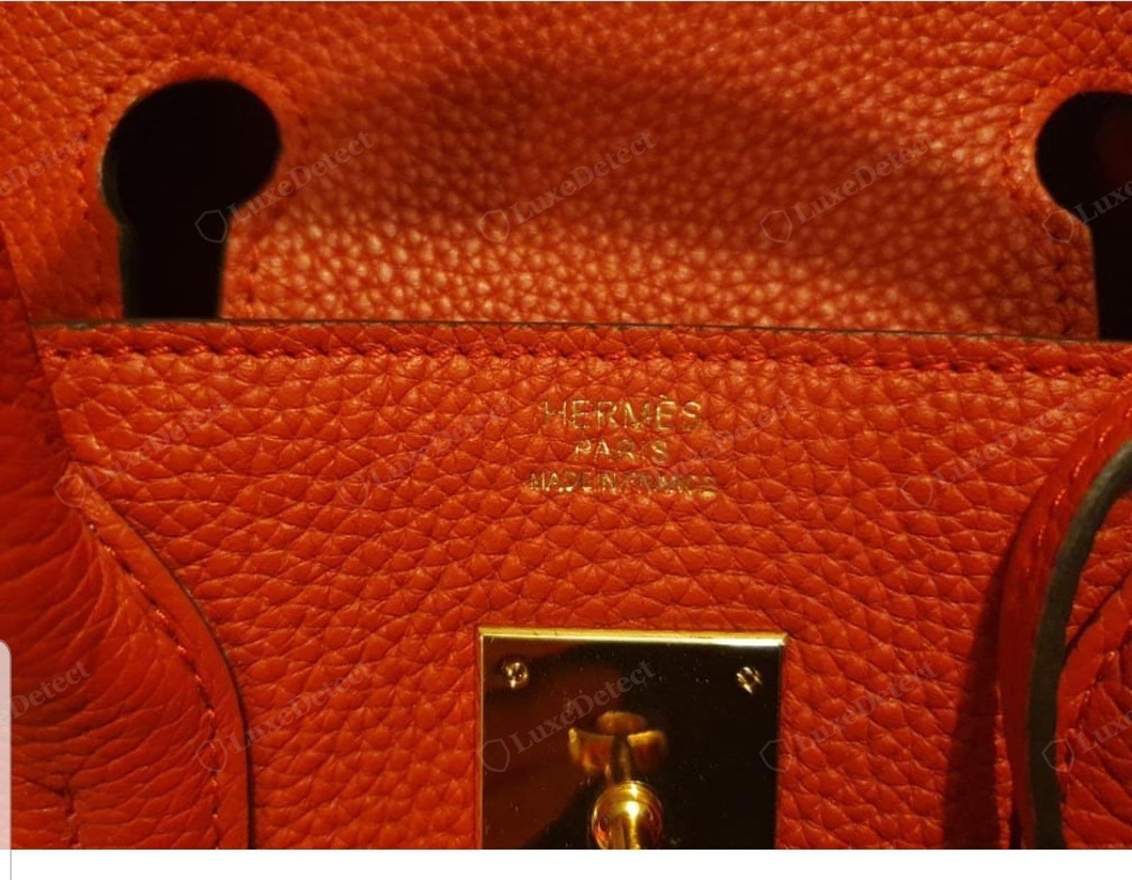 Counterfeit Hermès leather — orange grained calf with an over-uniform emboss; the "HERMÈS / PARIS / MADE IN FRANCE" gold stamp above it is faded and patchy with letters half-missing